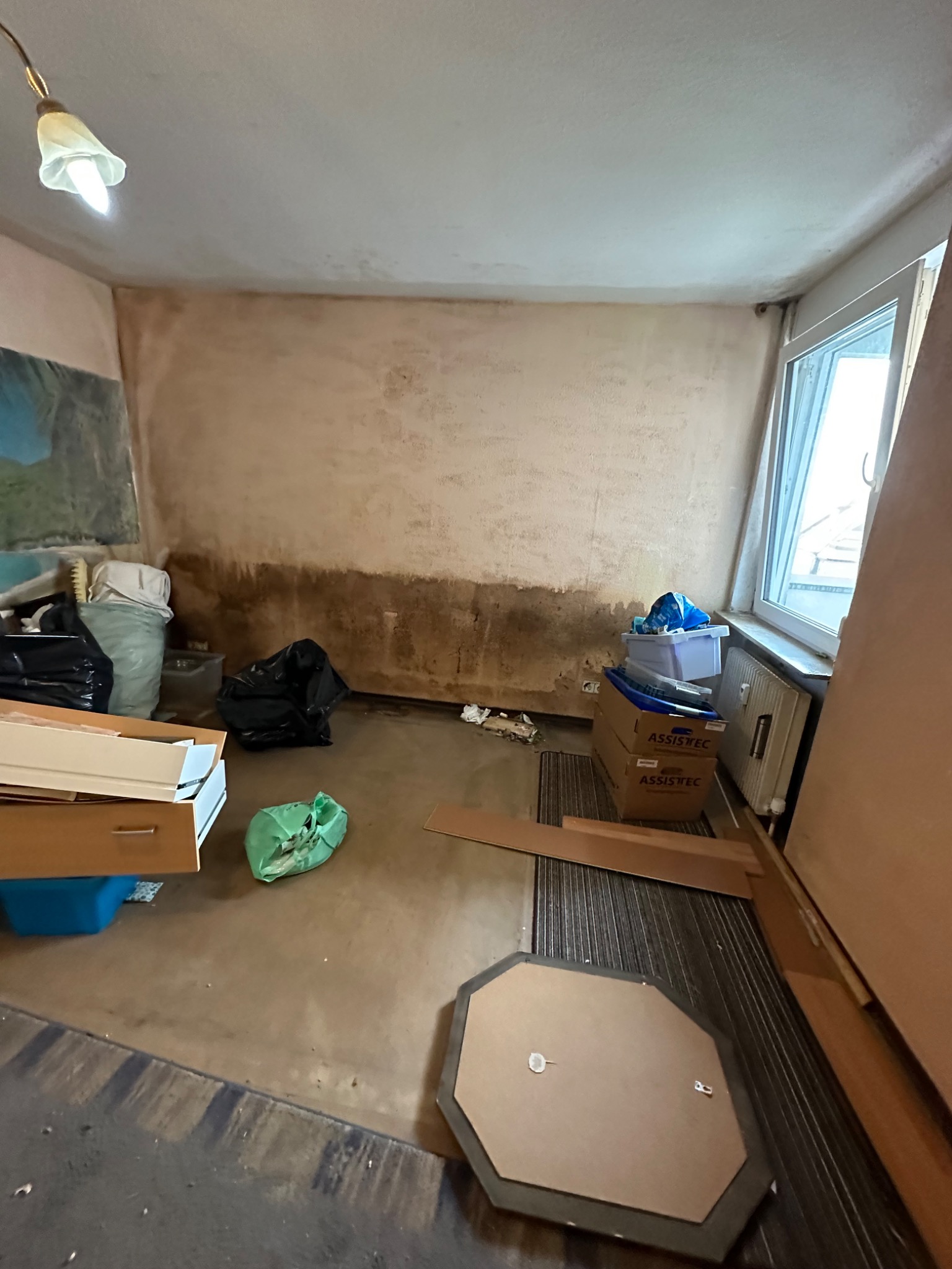 Freigeräumter Raum mit sichtbaren Feuchte- und Verfärbungsspuren an der Wand